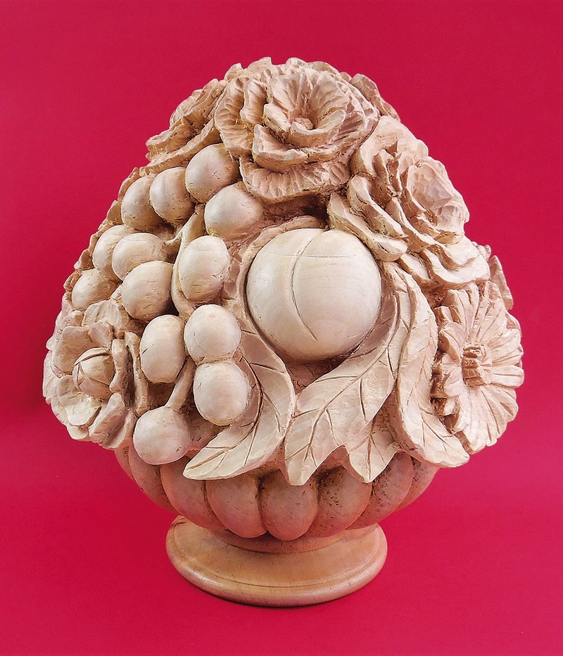 Wooden carving of fruit and flowers on red background.