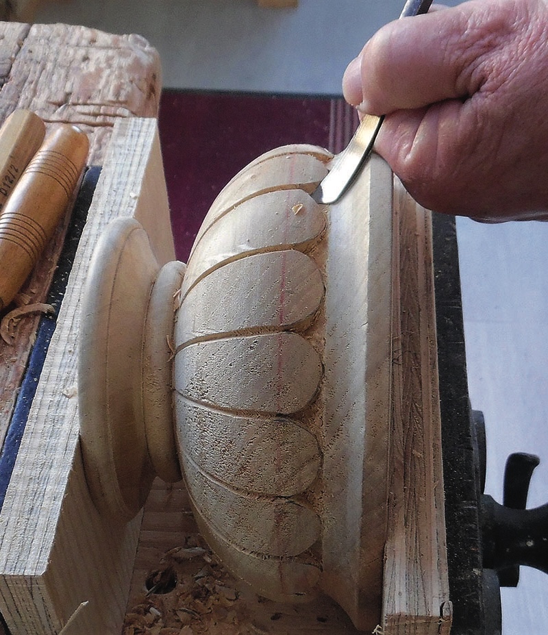 Hand carving wooden spindle with chisel tool.