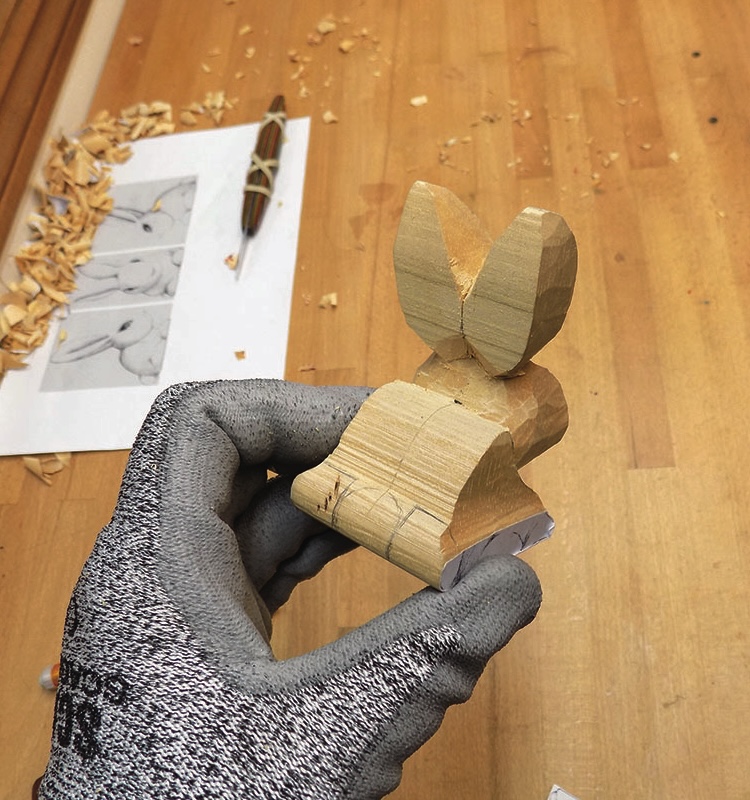 Hand holding carved wooden rabbit sculpture.
