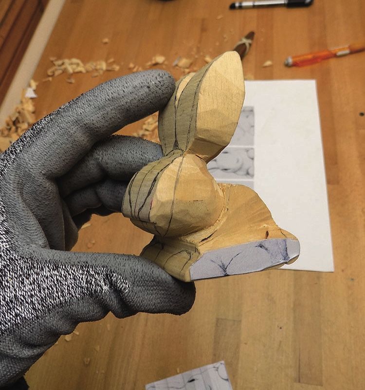 Hand holding carved wooden rabbit sculpture in progress