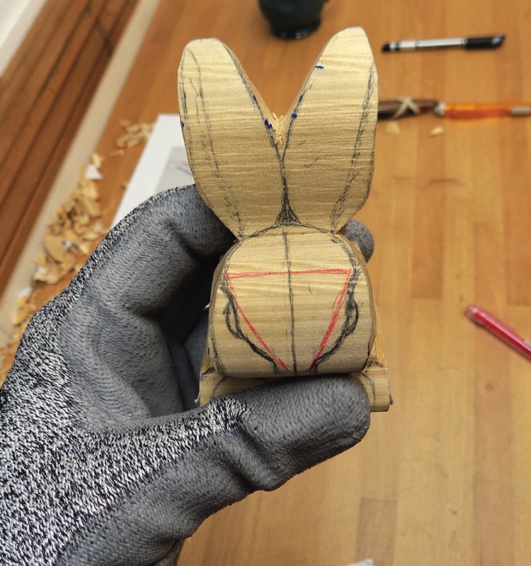 Gloved hand holding carved wooden rabbit figure.