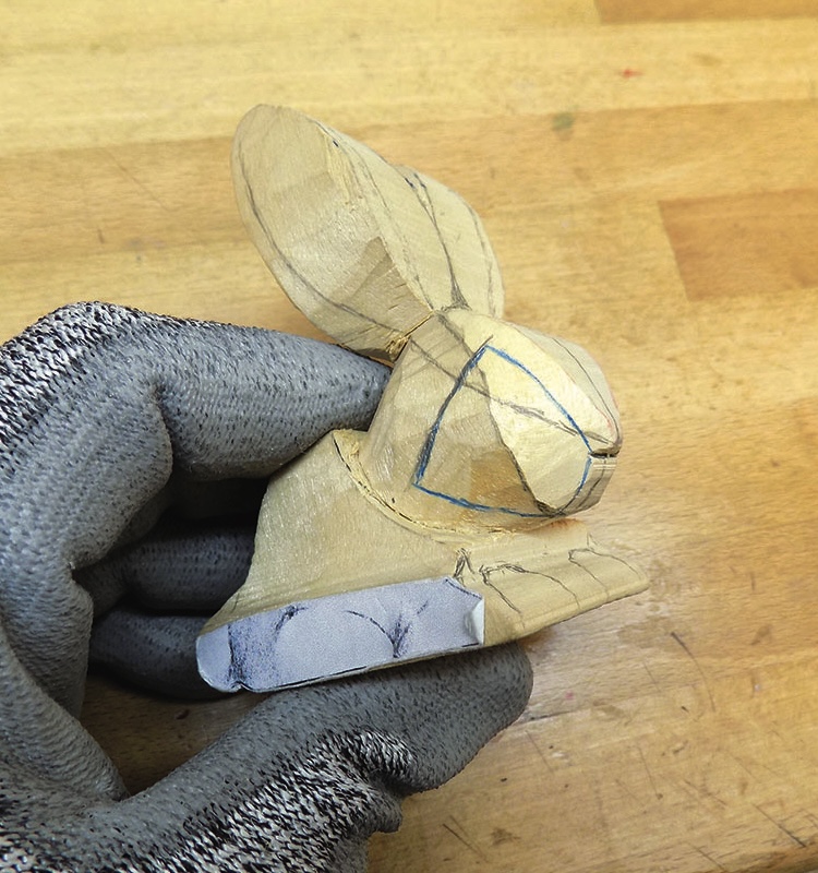 Hand holding wooden rabbit carving in progress.