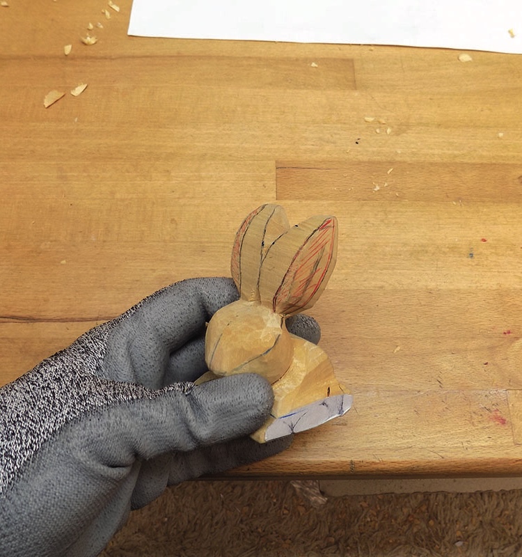 Gloved hand holding a carved wooden rabbit figure.