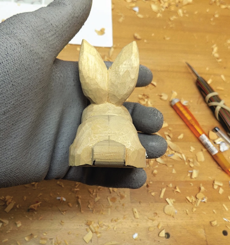 Hand holding wooden rabbit carving on workbench.