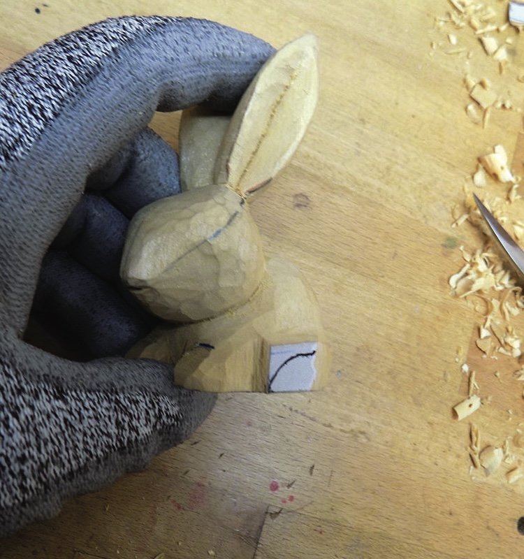 Gloved hand carving a wooden rabbit figure.