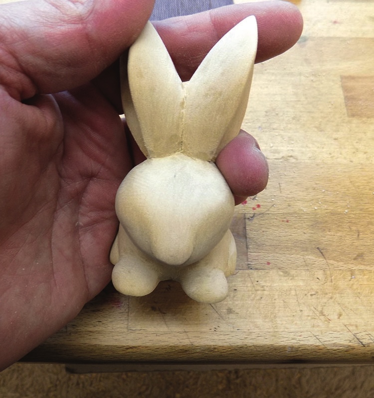 Hand holding small carved wooden rabbit figurine.