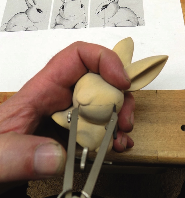 Carving a wooden rabbit sculpture with reference sketches.
