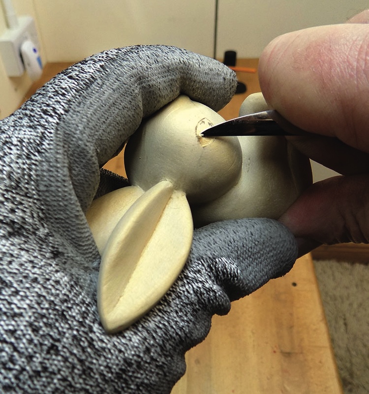 Gloved hand carving a wooden figurine.