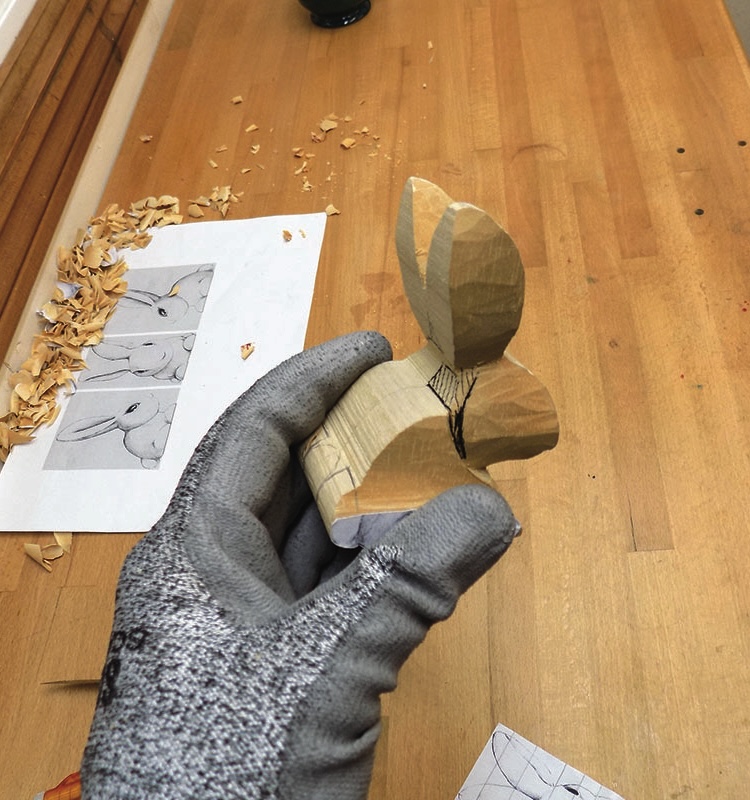 Hand carving wooden rabbit sculpture on workbench.