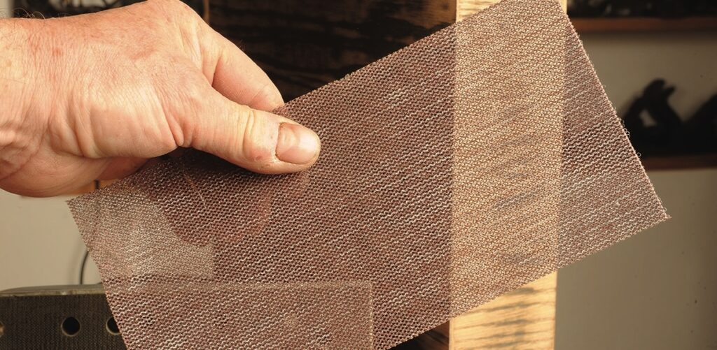 Hand holding abrasive sanding mesh sheet.