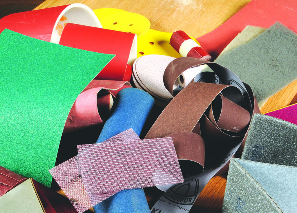 Various coloured sandpaper sheets and rolls on table.