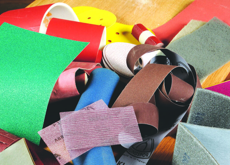 Various coloured sandpaper sheets and rolls on table.