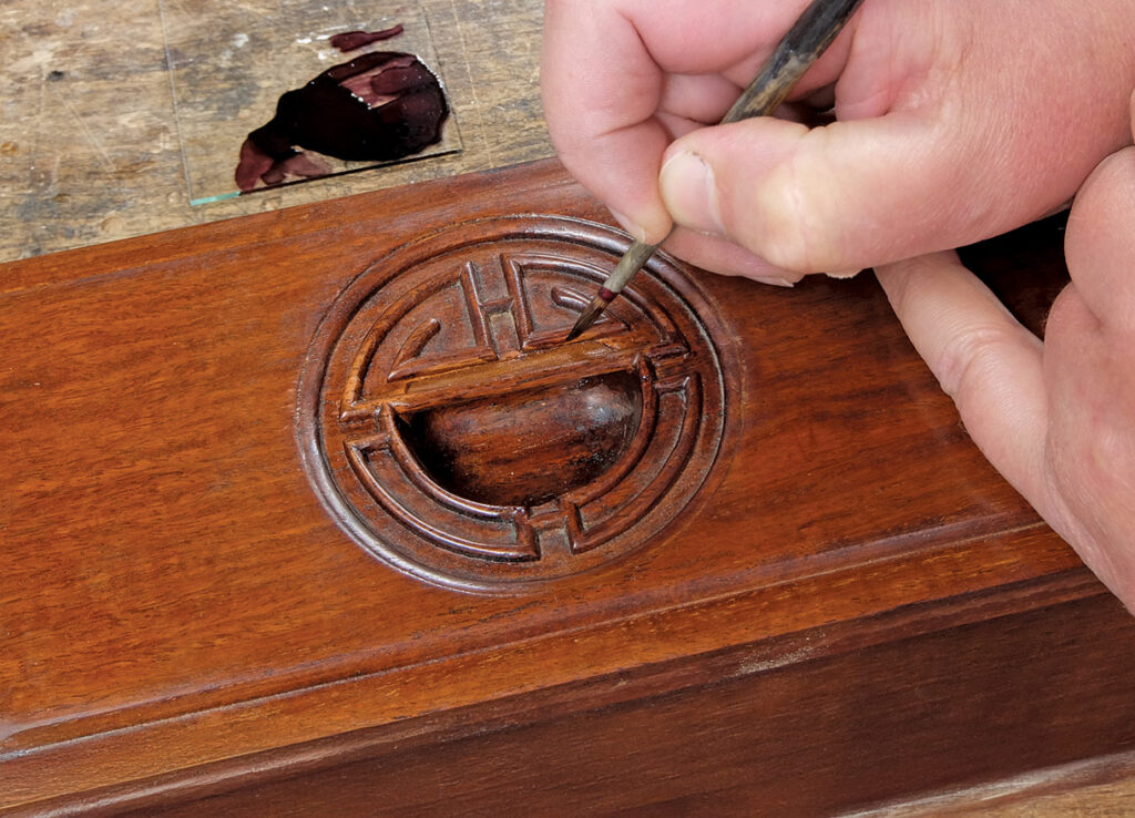 Hand painting intricate wood carving with brush