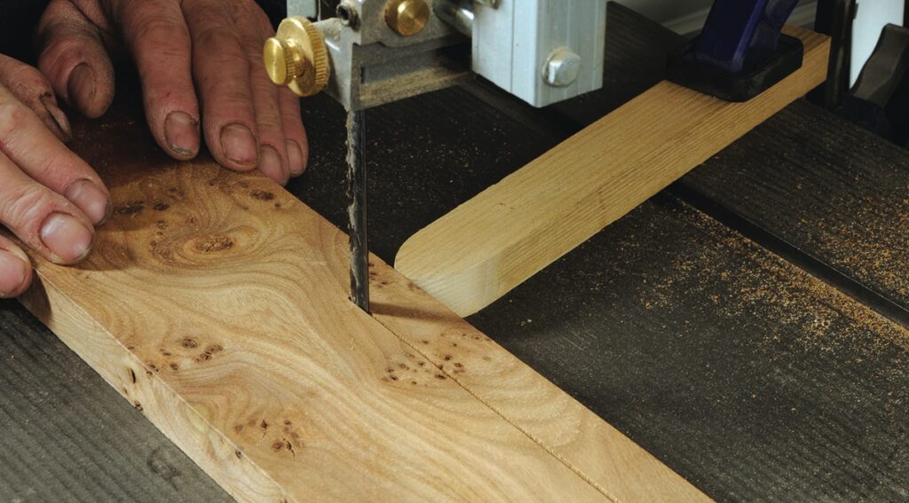 Person cutting wood with bandsaw machine.