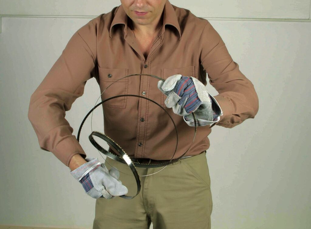 Man handling coiled metal blade with gloves.