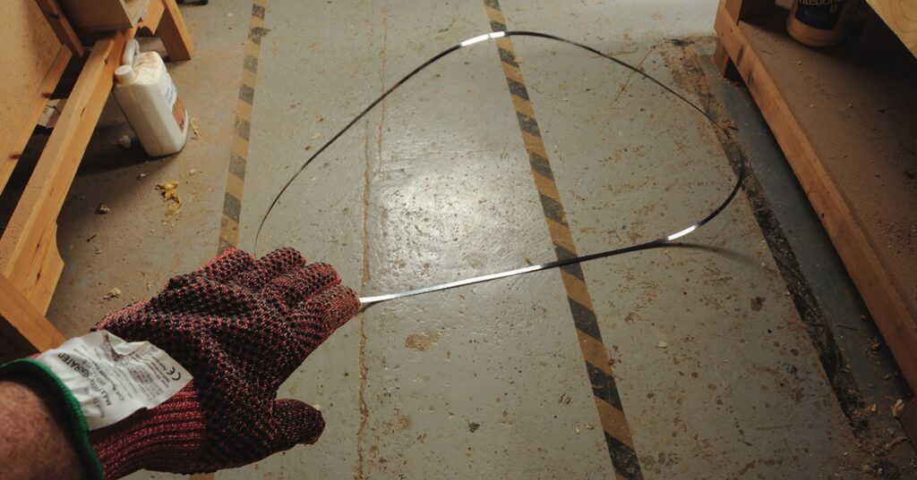 Gloved hand holding flexible metal strip on floor.