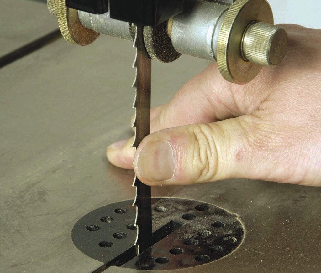 Hand adjusting bandsaw blade tension on table.