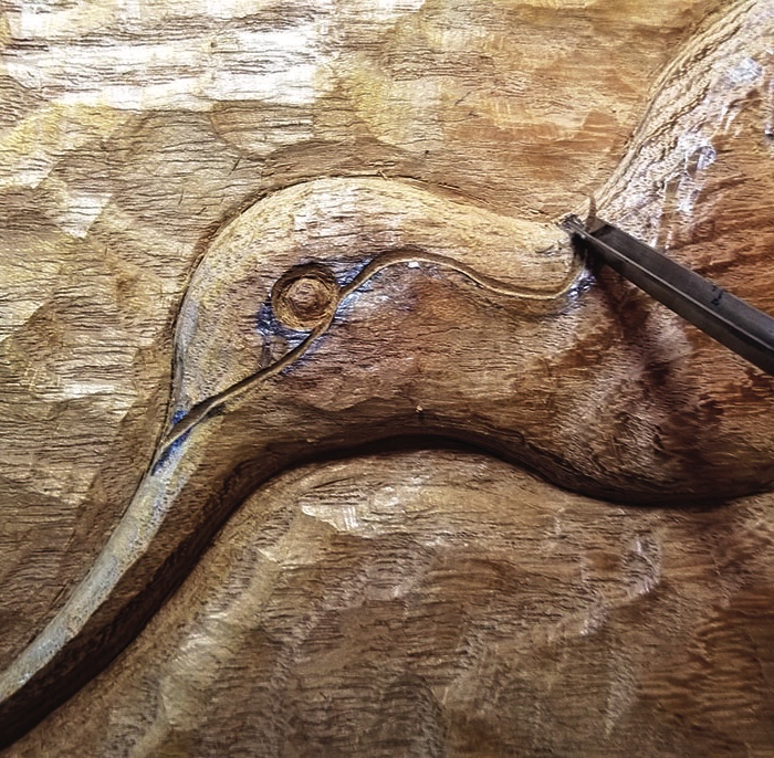 Sculptor chiseling detailed bird design into wood