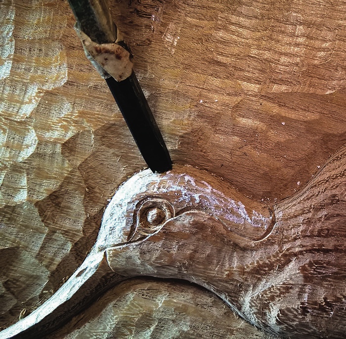 Wood carving of bird being detailed with chisel.