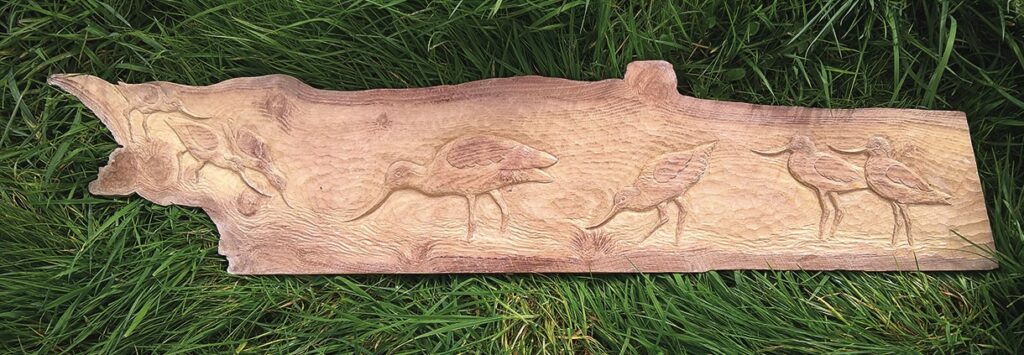 Wooden carving of birds on grass.