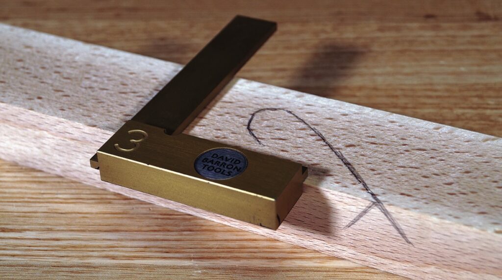 Brass woodworking square on wood with pencil mark.