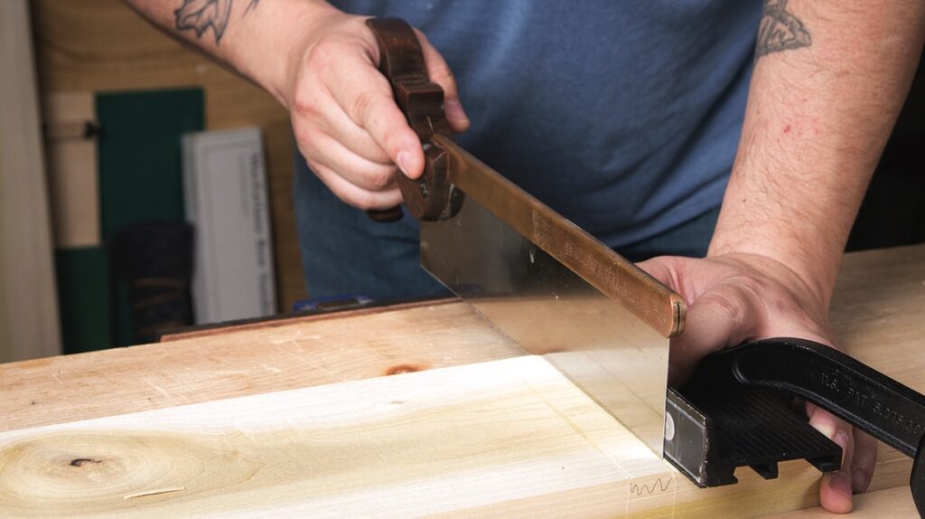 Person sawing wood with handsaw on workbench.