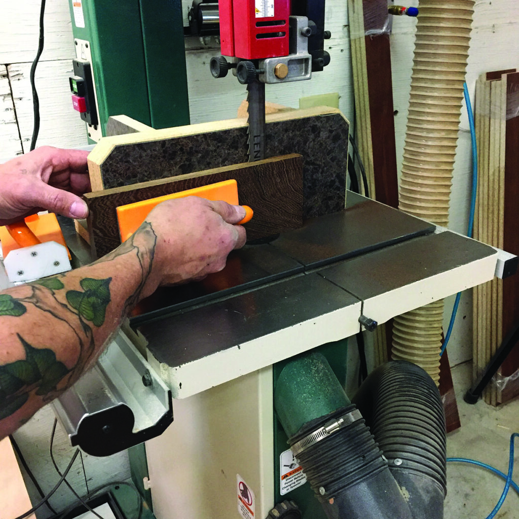 Man using bandsaw to cut wood piece.
