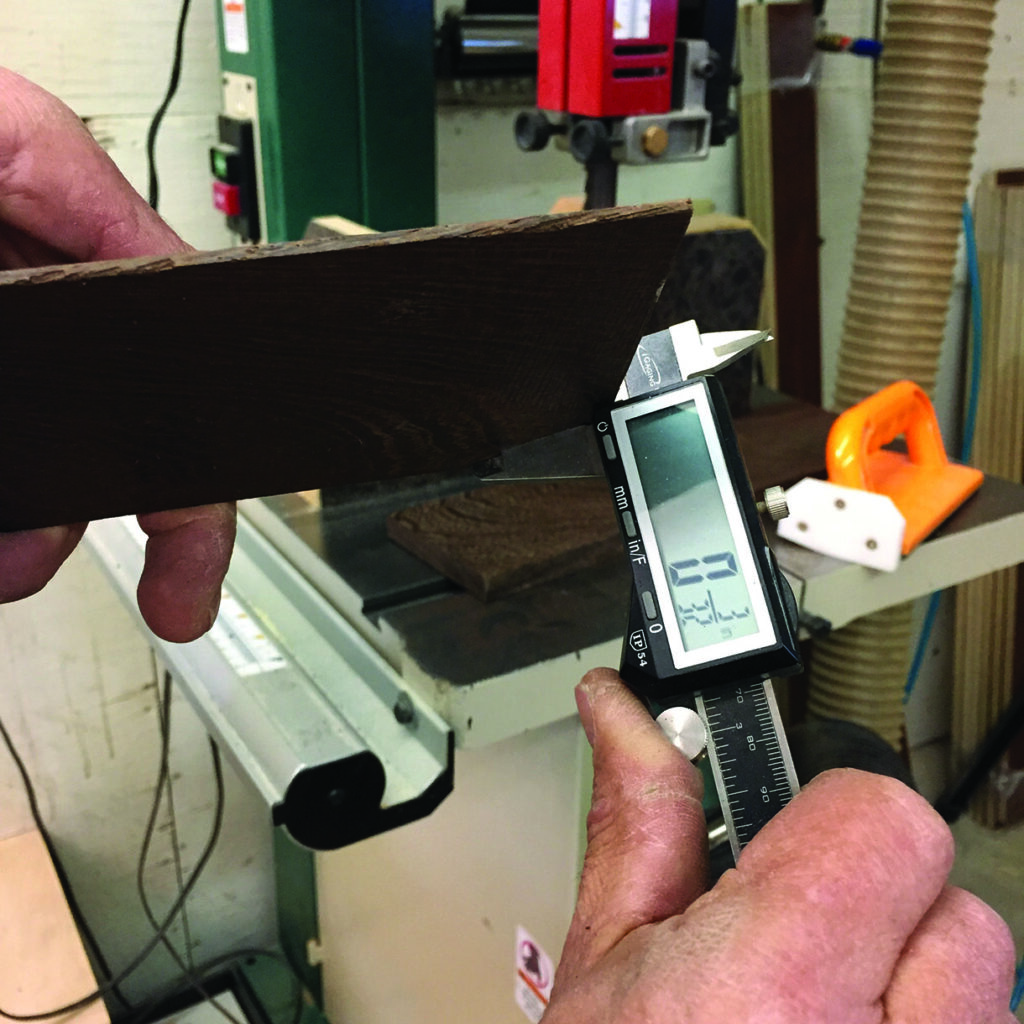 Measuring wood thickness with digital caliper in workshop.