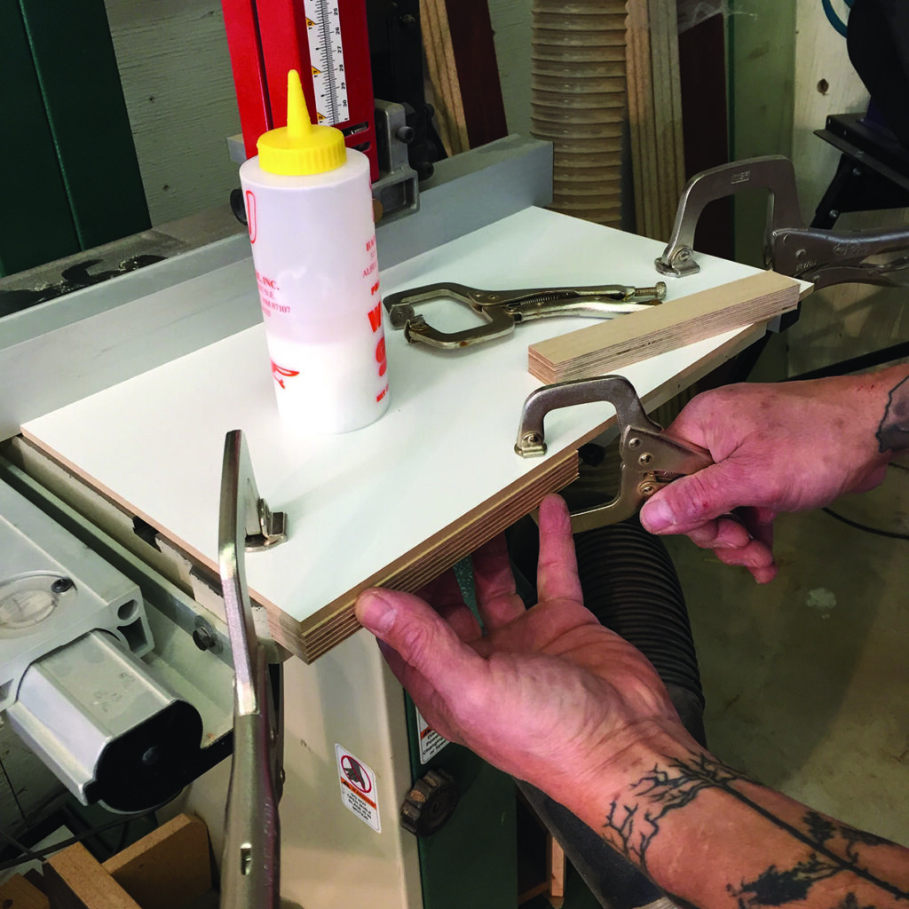 Person clamps wood piece with glue in workshop.