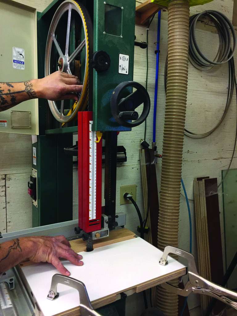 Person adjusting woodworking bandsaw machine in workshop.