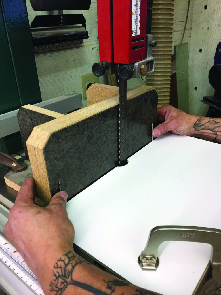 Person using bandsaw to cut wood piece.