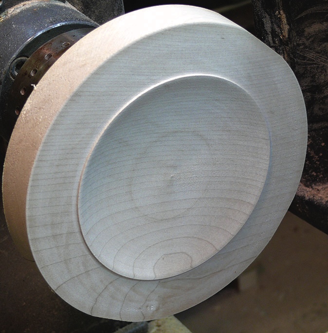 Wood lathe creating a round wooden plate.