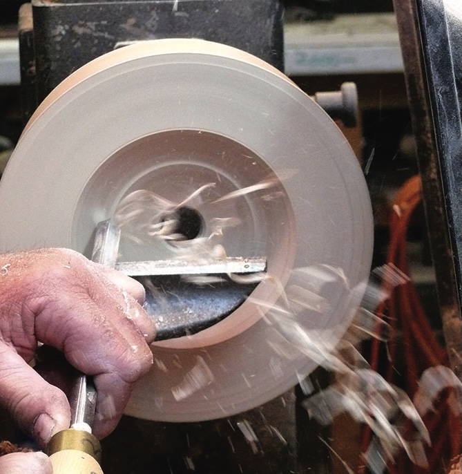 Person turning wood on a lathe, creating shavings.