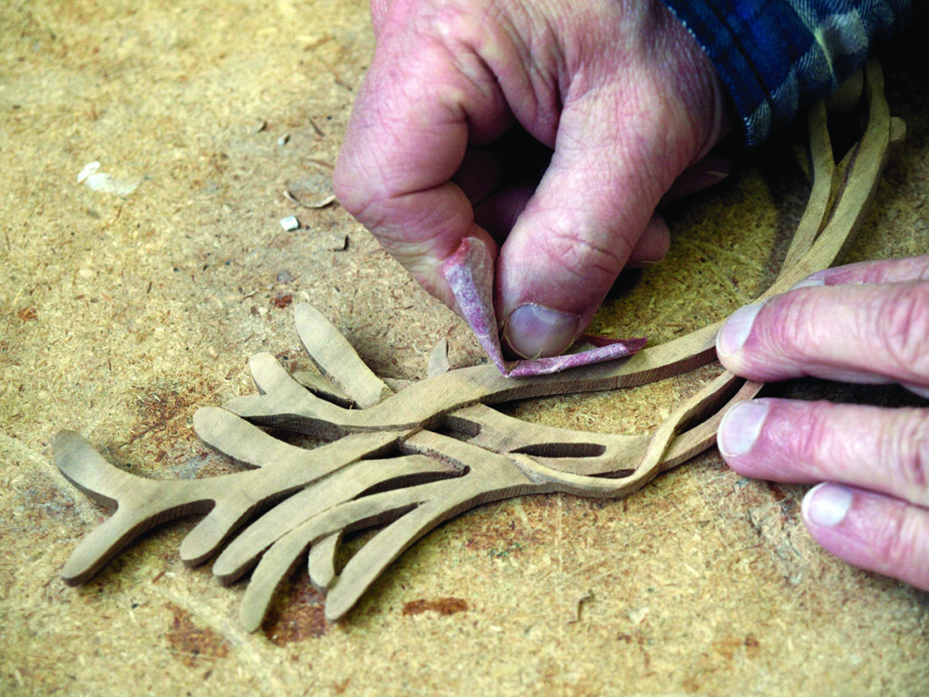 Person sanding intricate wooden carving detail.