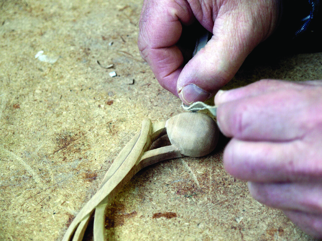 Hands carving wooden spoon on workbench.