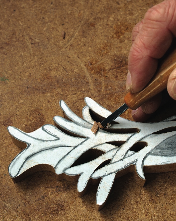 Hand carving intricate wood design with chisel.