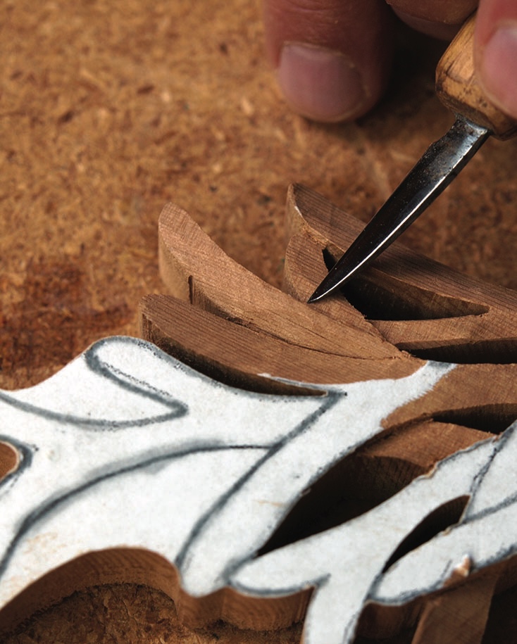 Hand carving intricate wood design with chisel.