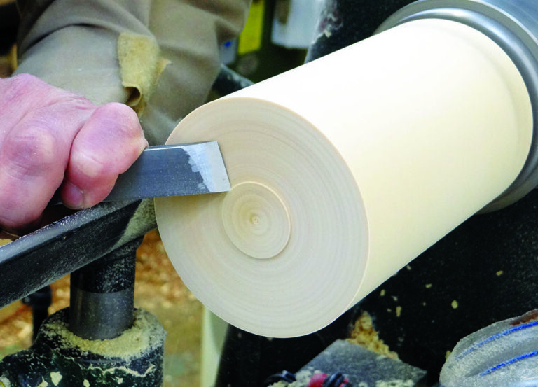 Person using chisel on spinning wood lathe.