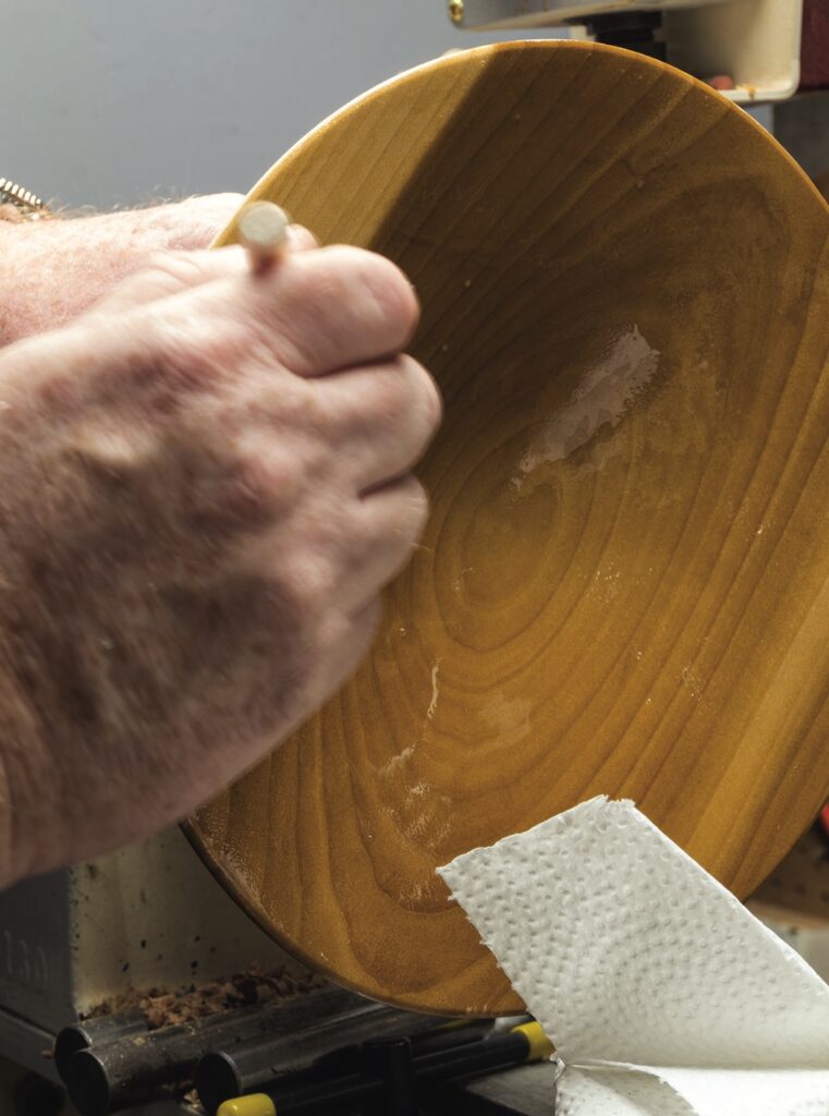 Craftsman sanding a wooden bowl on a lathe.