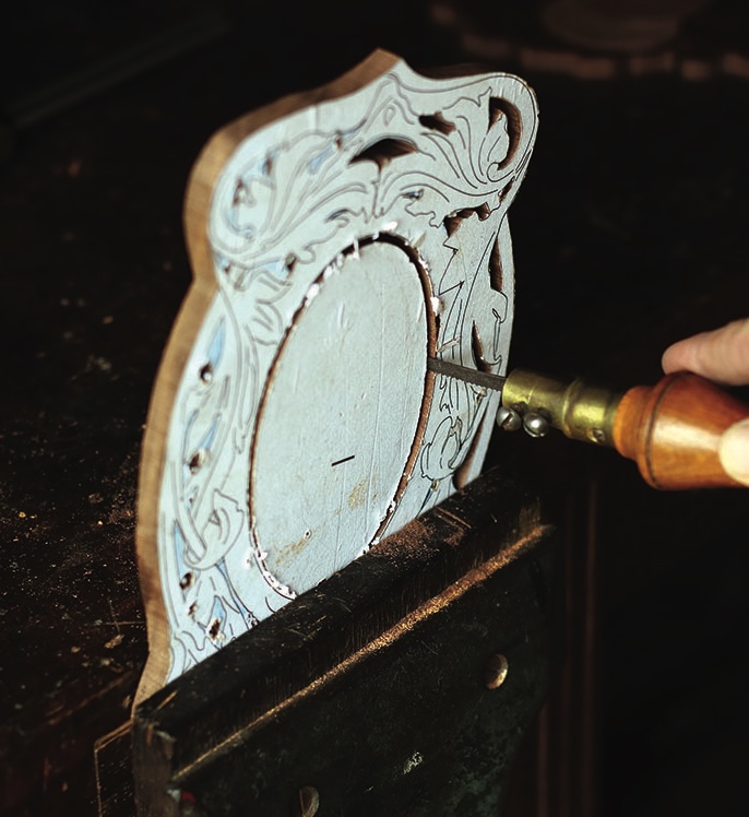 Hand carving intricate wood design with a tool.