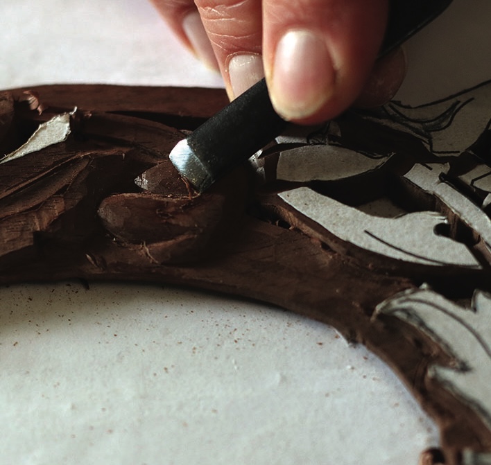 Close-up of hand carving intricate wood design.