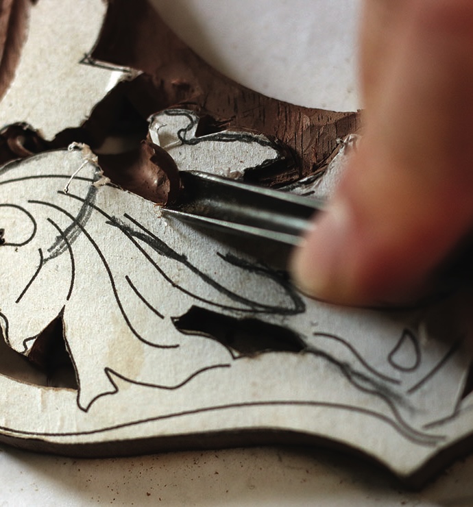 Person carving intricate wood design with tool.