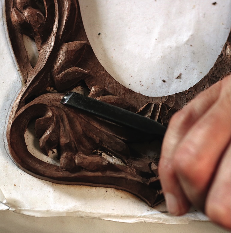 Hand carving intricate wood design with chisel tool.