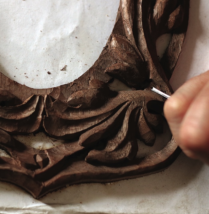 Hand carving intricate wooden design with tool.