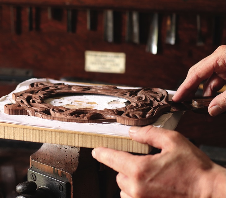 Craftsman carving detailed wooden frame by hand.