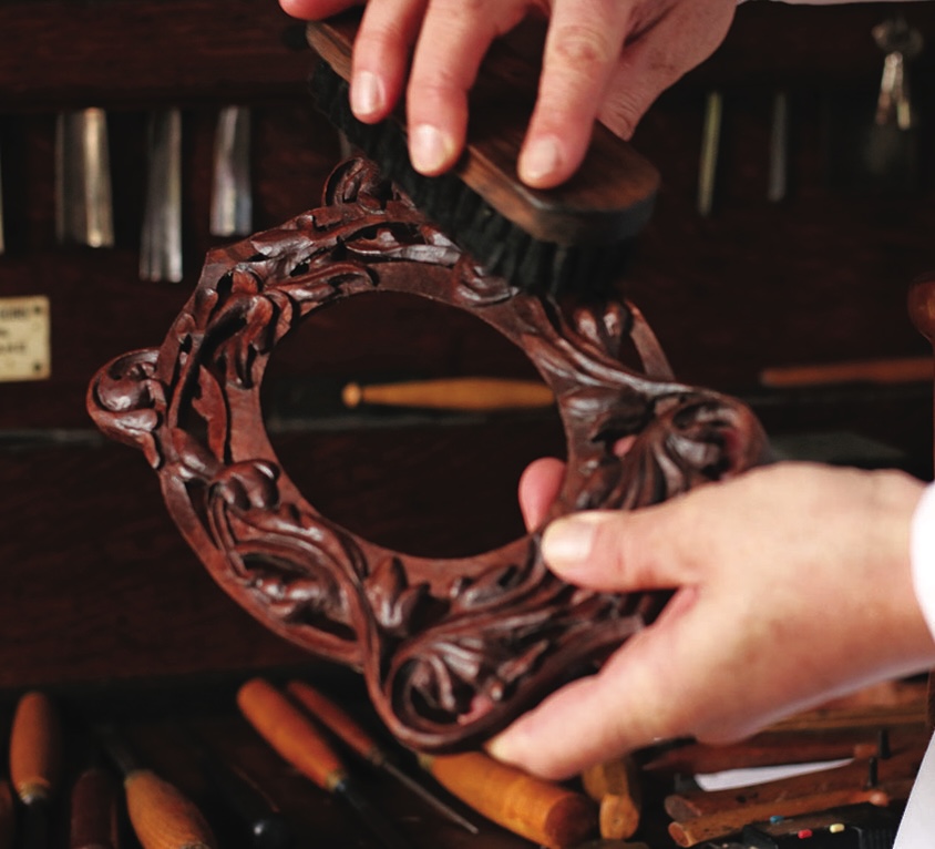 Hand brushing intricate wooden frame with tools nearby.