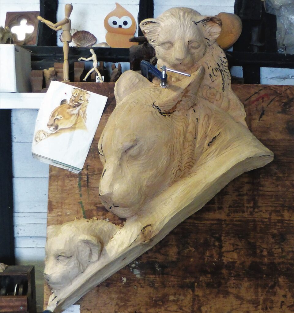 Wood carving of lioness and cubs in workshop.