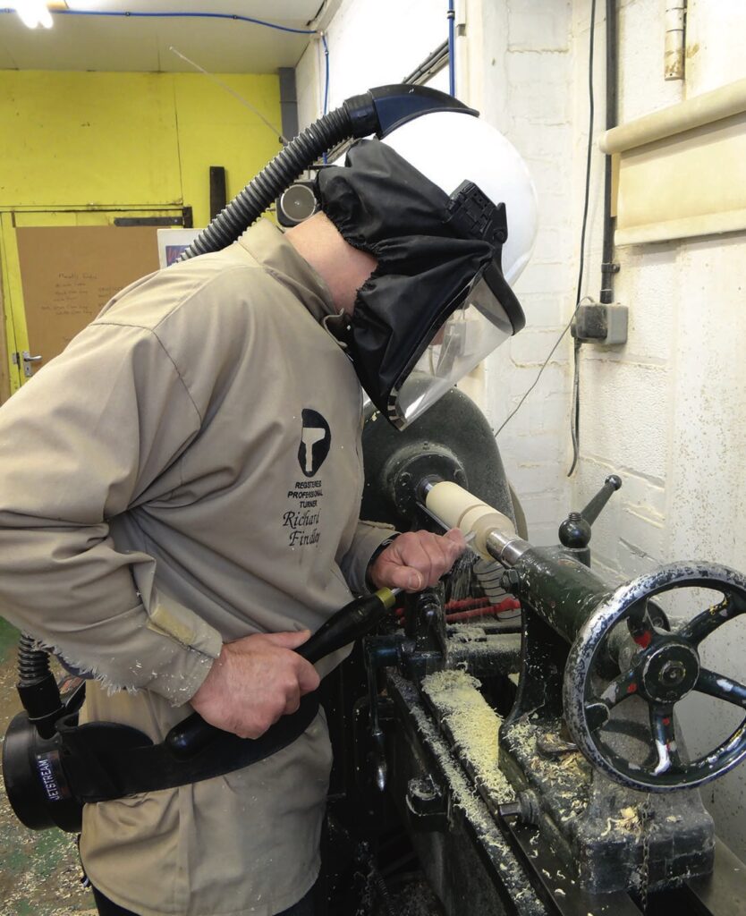 Woodturner wearing safety gear working on lathe machine.
