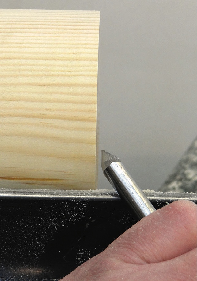 Hand holding chisel carving a wooden cylinder