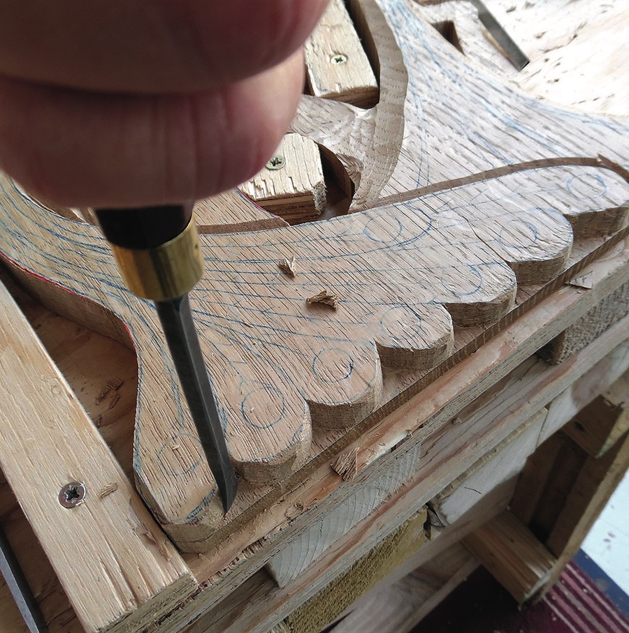 Hand chiseling intricate wood carving detail.